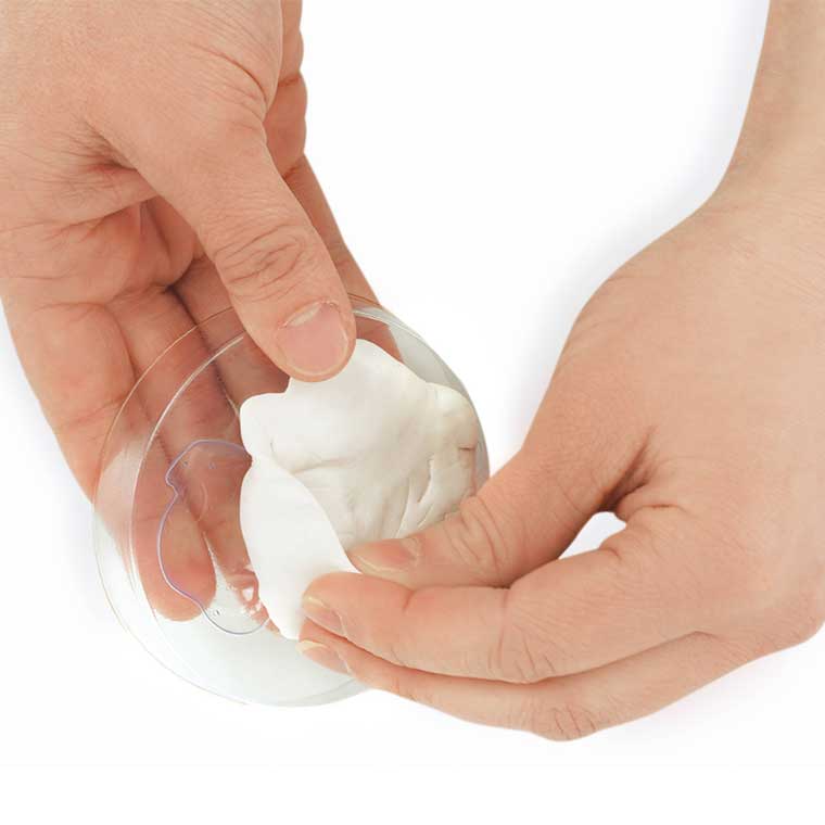 Two hands removing white putty from a plastic mold.