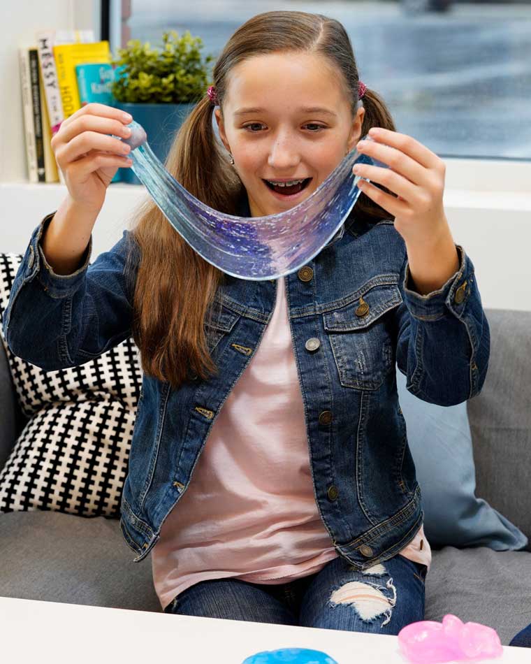 Girl sitting on a couch in front of a table, stretching translucent blue putty.