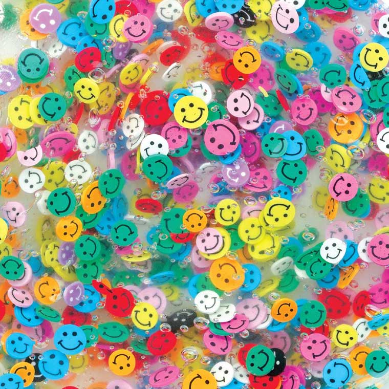 Close up of clear putty with clay pieces shaped smiley faces mixed into it.