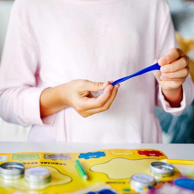 Two hands holding blue putty stretching and mixing with instruction mat on table.