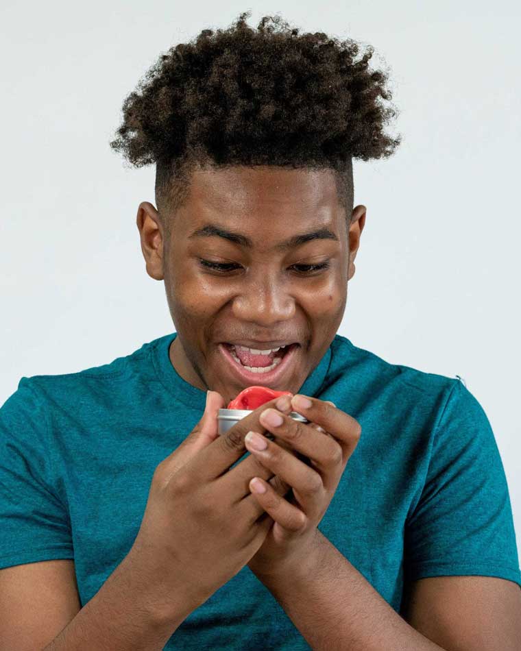 Man holding and smelling a tin of red cinnamon scented Thinking Putty®.