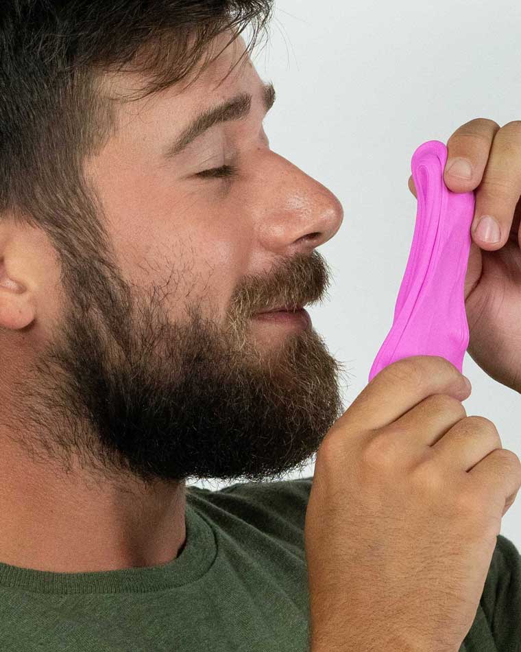 Man holding bright violet putty and smelling the floral scent.
