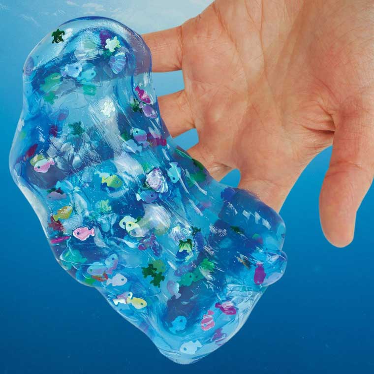 Hand holding stretched translucent blue putty with sea creature pieces in it.