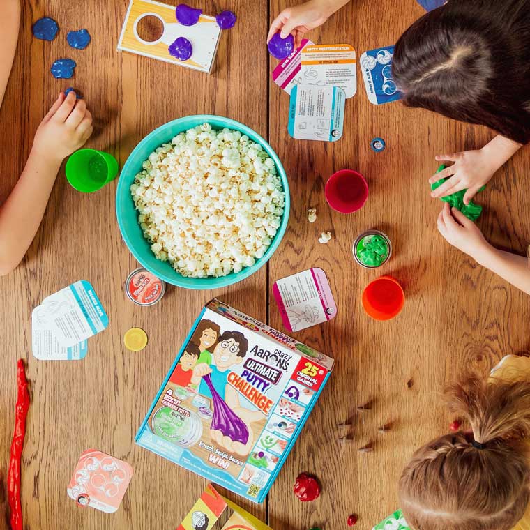 Seen from above, three people playing Ultimate Putty Challenge with a bowl of popcorn on the table.